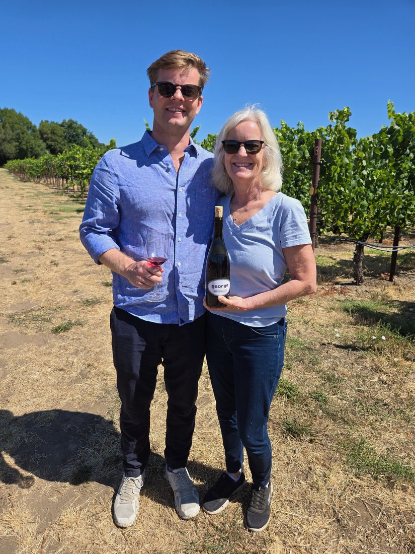 Collin and Laura with a bottle of George Pinot Noir between vineyard rows